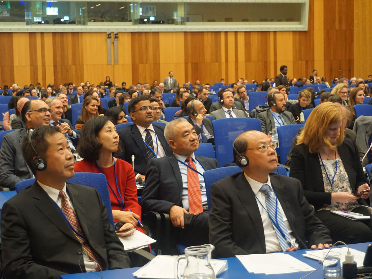 Formally dressed participants sitting in a large room and listening very carefully to speakers.