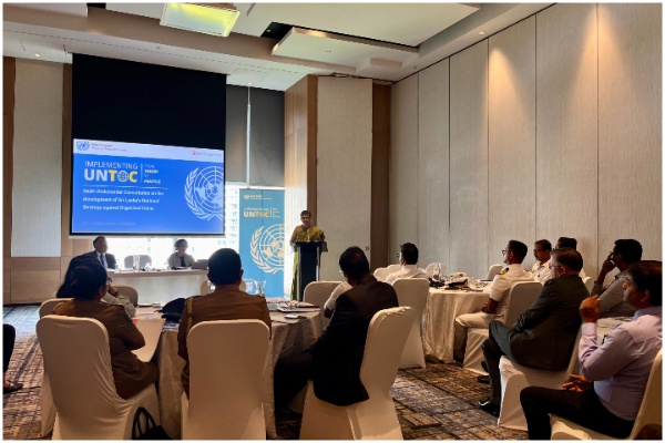Participants looking towards the main speaker, with a screen depicting an e-banner on UNTOC in the background.