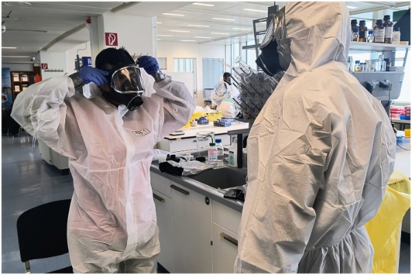 Two participating officials facing each other, as they don PPE kits and safety gear.